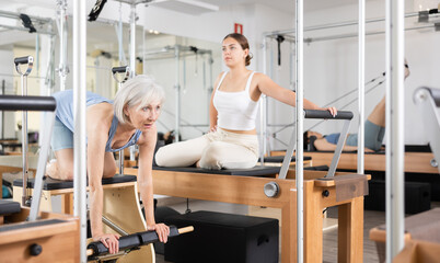 Smiling elderly woman in sportswear training pilates performer bed in gym