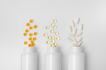 Three blank jars with yellow, orange and white capsules pills on a gray isolated background....