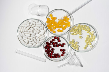 Four dishes with labware and pills capsules in yellow, white, red and orange colors on a white isolated background. Dietary supplements, scientific research, vitamins for improving health concept