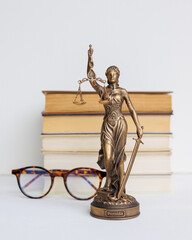 Themis goddess of justice statuette on light background on table with books and glasses. legal company, university judicial structure. bar association and human rights defenders, court acquittal