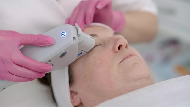 female client gets soothing SMAS ultrasound face lifting massage at a beauty center using professional equipment. close up face 