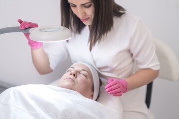 Obraz na płótnie Canvas close up skilled esthetician performs facial treatments, such as peels and lifting massages, using lamp to see skin problems at an aesthetic medicine clinic