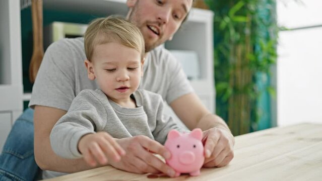 Father and son inserting coin on piggy bank sitting on table at dinning room