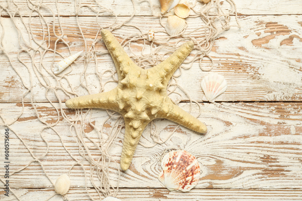 Wall mural Beautiful starfish with seashells and net on light wooden background