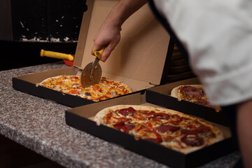 Close up of anonimous pizza chef slicing appetising pizza with cutter wheel in order to be served...