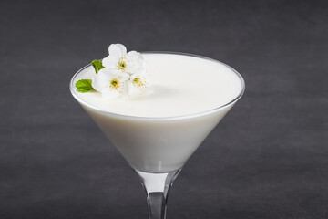 Vanilla cream jelly, Panna Cotta, decorated with small white flowers, in a martini glass. Dark gray background. Close-up