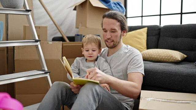 Father and son writing on notebook sitting on floor at new home