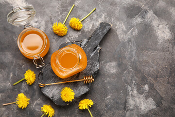Board with jars of dandelion honey on dark grunge background