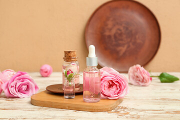 Bottles of cosmetic oil with rose extract and flowers on light wooden table