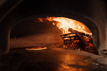 Pizza concept. Preparing traditional italian pizza. Long shovel for pizza, baking dough in a professional oven with open fire in interior of modern restaurant kitchen. High quality photo
