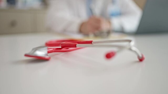 Young hispanic man doctor writing on clipboard at clinic