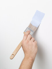 Hand with blue paint brush painting a white wall