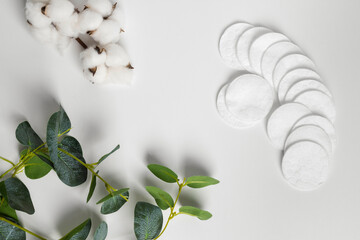 Cotton pads decorated with a plant leaves and cotton flowers lying on a white background. flat lay, top view, copy space. © Georgi