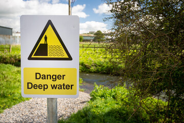 Danger Deep Water warning sign close up by rural waterway river stream. Beware falling in, drowning.