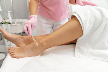 Obraz na płótnie Canvas Application of a special gel with a wooden stick on a woman's leg before laser hair removal. Laser epilation, hair removal concept. Cosmetological procedures in the salon