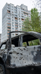 A burnt car with shrapnel holes in front of a house with broken windows after Russia's biggest missile attack on Kyiv, the concept of Russia's war against Ukraine, the genocide of the Ukrainian people