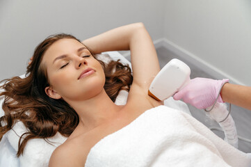 Beauty procedure. Hair removal by laser hair removal. Caucasian young woman lies on the couch with...