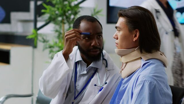 Asian patient with cervical collar doing brain damage exam with african american medic, checking concussion and having medical appointment. Person with neck fracture and brace in hospital lobby