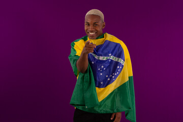 Black-skinned man holding the flag of Brazil and wearing the shirt of the Brazilian soccer team in studio photo