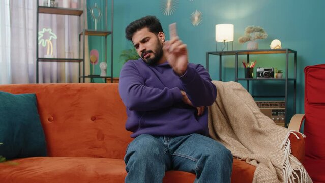 Displeased upset indian man reacting to unpleasant awful idea, dissatisfied with bad quality, wave hand, shake head No, dismiss idea, dont like proposal. Young hindu guy at home apartment room on sofa
