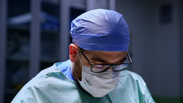 Male bearded mid-aged doctor working in the surgery room. Close-up portrait of a surgeon focused on work.