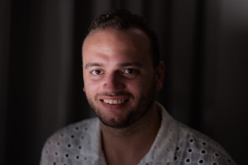 Fototapeta premium Posing against a dark curtain, a Middle Eastern man expresses a joyful smile and direct gaze at the camera.