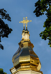 Gilded dome with a cross of an Orthodox church against a blue sky with white clouds