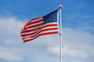An American flag flapping in the wind against a blue sky with white clouds.