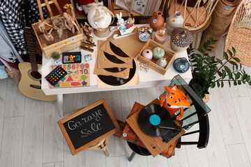 Sign Garage Sale written on blackboard near many different stuff indoors, above view