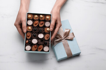 Woman with open box of delicious chocolate candies at white marble table, top view