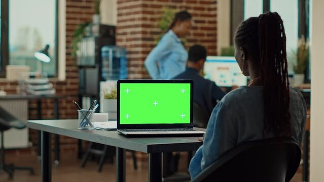 Corporate person using green screen in office, checking business information on isolated display. Young woman working with chroma key coyspace on laptop, blank mockup template.