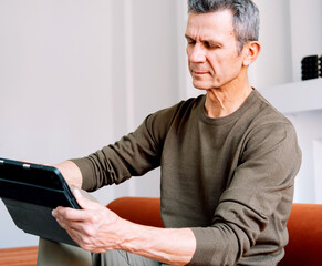 Fototapeta premium Mature caucasian man websurfing on digital tablet at home. Lifestyle, people and tehnology concept