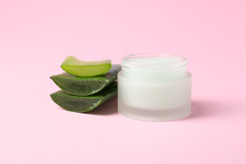 Jar of natural gel and cut aloe on pink background, closeup