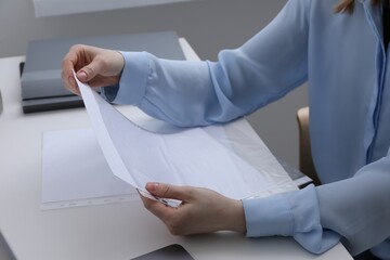 Woman putting paper sheet into punched pocket at white table, closeup