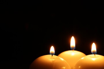Burning wax candles on black background, closeup. Space for text