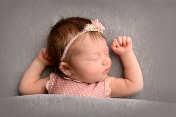 A cute little newborn baby in a pink suit and a pink headband with a butterfly on his head sleeps sweetly. Professional macro photo on a grey background.