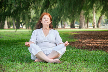 Portrait of a mature latin woman in white clothes practicing yoga and meditating outdoors in a park. Concepts: wellness, tranquility and healthy lifestyle.