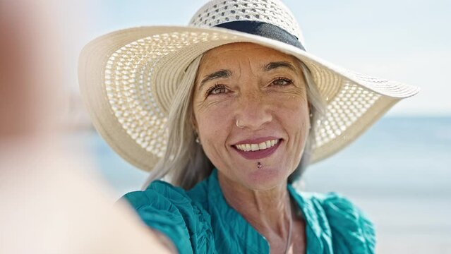 Middle age grey-haired woman tourist making selfie by the camera kissing at beach