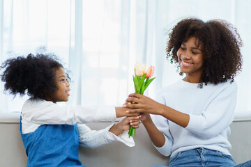 Lovely cute little girl gives her mother a beautiful bouquet of flower in the international Mother's Day, American - African black ethnic family portrait. International Mother's Day concept.