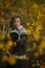 Caucasian female photographer using camera with telephoto lens in yellow autumn forest