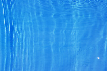 Blue water with ripples on the surface. Defocus blurred transparent blue colored clear calm water surface texture with splashes and bubbles. Water waves with shining pattern texture background.
