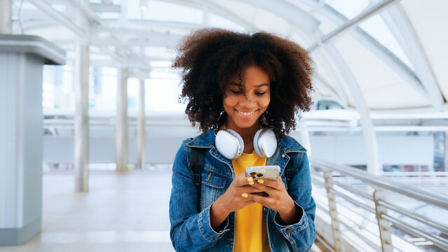 Happy Young Afro Woman Listening To Playlist Music With Wireless Headphones While Wearing Yellow Shirt And Jeans Jacket Outdoor