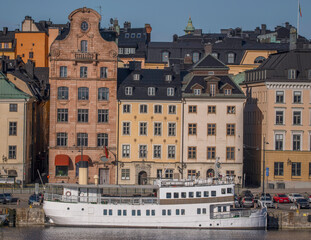 Old 1700s houses on the pier Skeppsbron in the old town Gamla Stan, an archipelago commuting ferry, a sunny early tranquil summer day in Stockholm