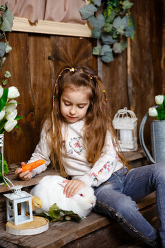 Laughing Child At Easter Egg Hunt With White Pet Bunny. Little Toddler Girl Playing With Animal. Girl Feeding Rabbit Carrot. Little Girl Playing With A Real Pet Rabbit. Cheerful Girl Looking At Rabbit