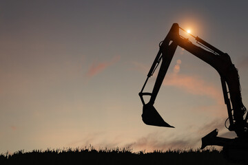 silhouette of a backhoe digger parked on the grass in the morning