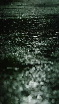 Closeup of rain drops falling on puddle with lights reflection on city sidewalk, Rain drop with street lights at night, Weather or environment, Nobody, Vertical video for smartphone footage