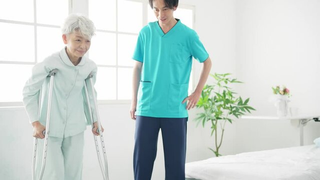 松葉杖で歩行訓練するシニア女性と介助するヘルパー