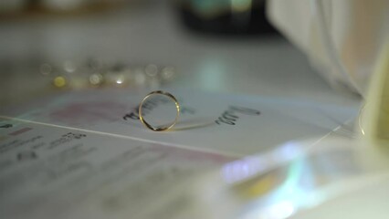 Two gold wedding rings roll together over cards, backlit with light as one ring rolls away from other, nobody. Concept of betrayal and parting at ceremony.