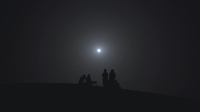 people gathering together under the full moon for a ceremony silhouette against the brightness of the moon 