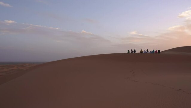 tourist walking on sand dunes desert at distance during colourful sunrise in Merzouga desert Marocco Africa